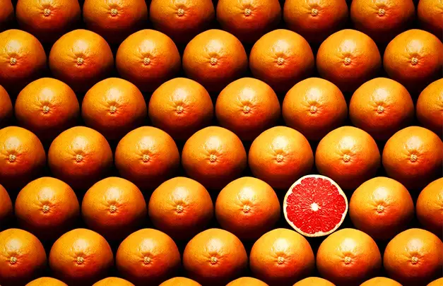 many rows of whole grapefruits with one sliced grapefruit